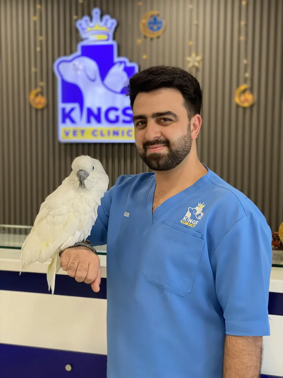 A Kings team member holding a white cockatoo in front of the clinic logo
